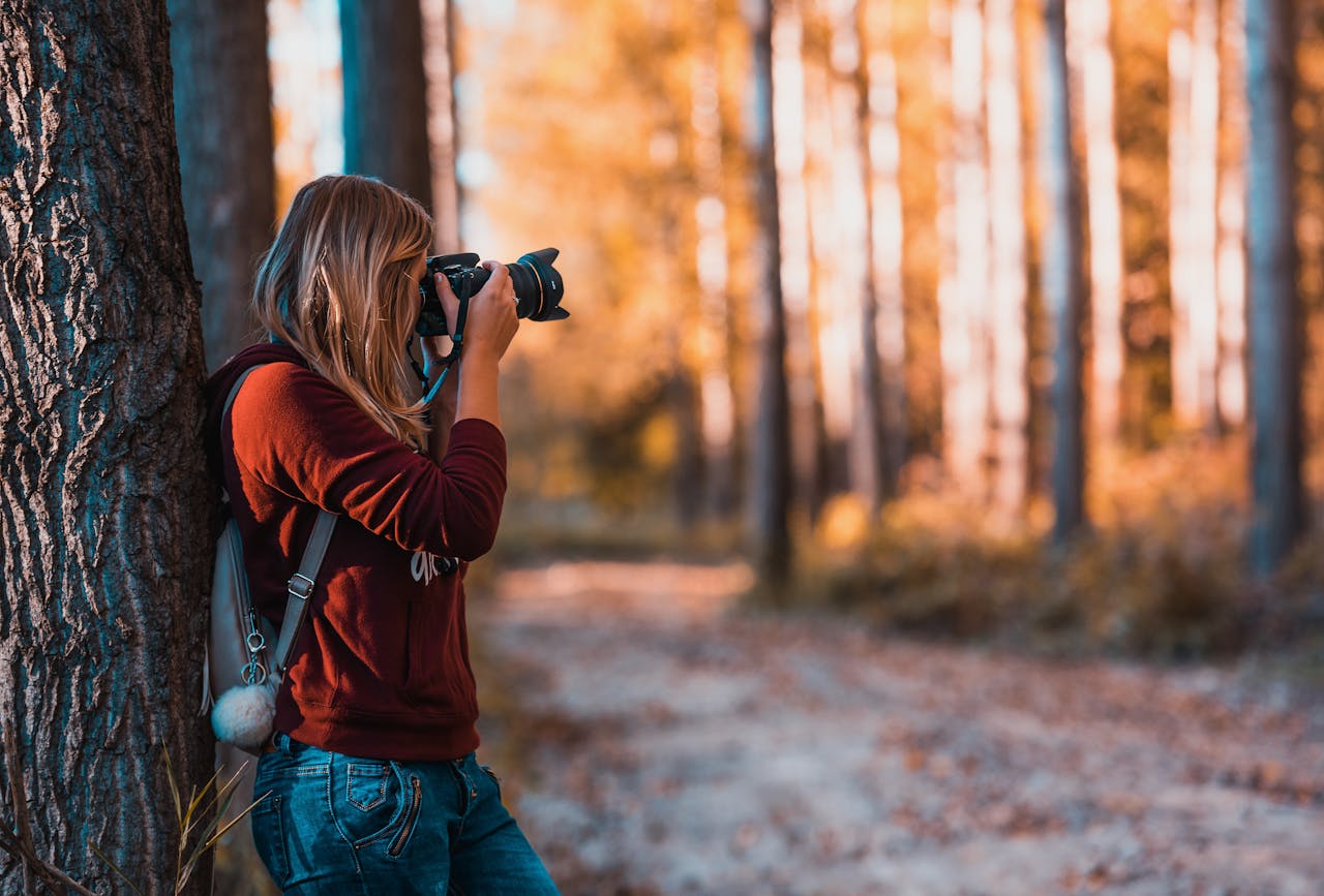 about-me A woman taking photos in an autumn forest, perfectly capturing the beauty of nature.